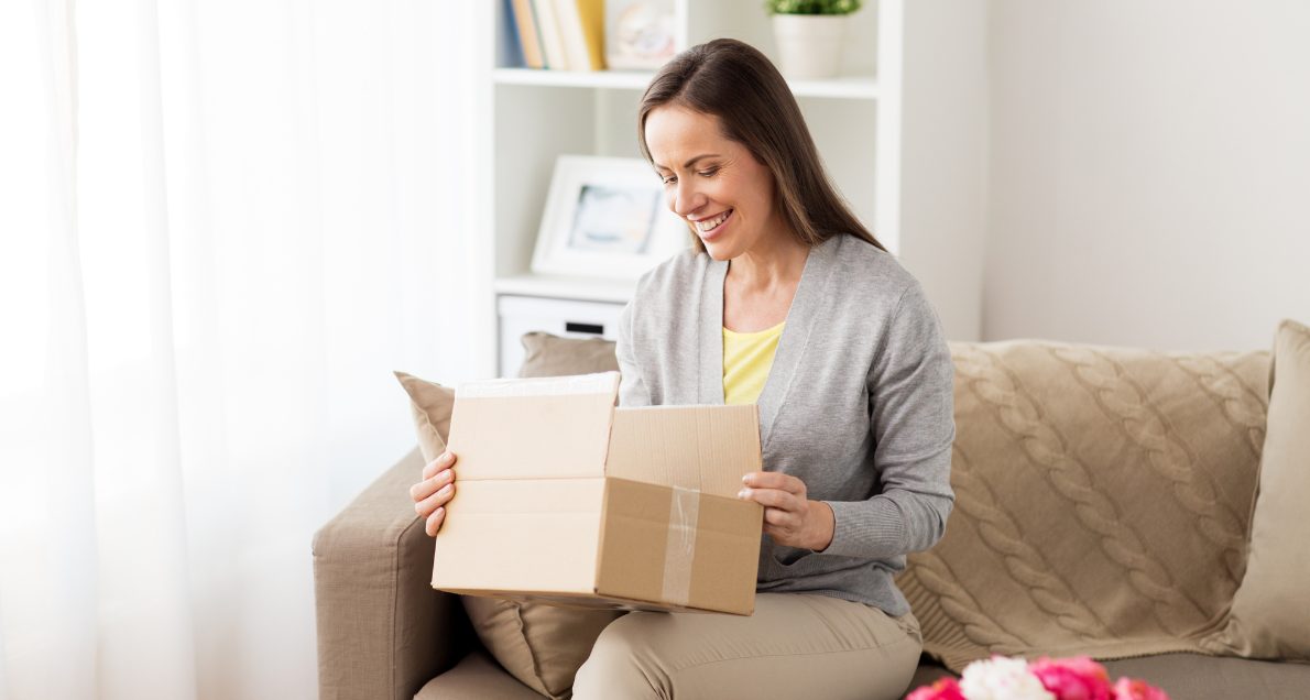 Smiling Woman Opening Cardboard Box on Her Couch