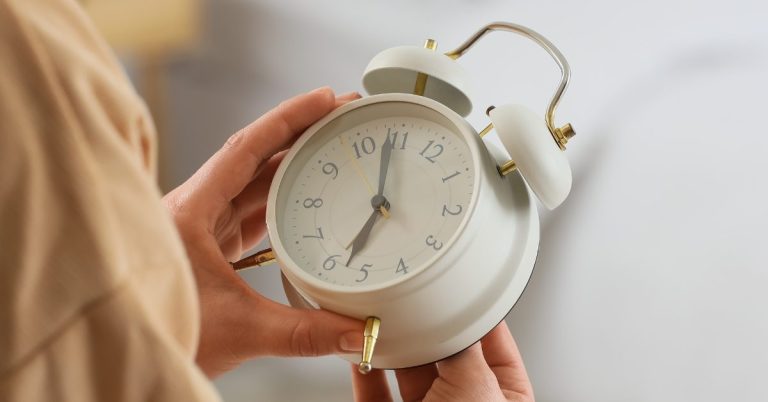 Woman Changing Clock for Daylight Saving Time in Bedroom